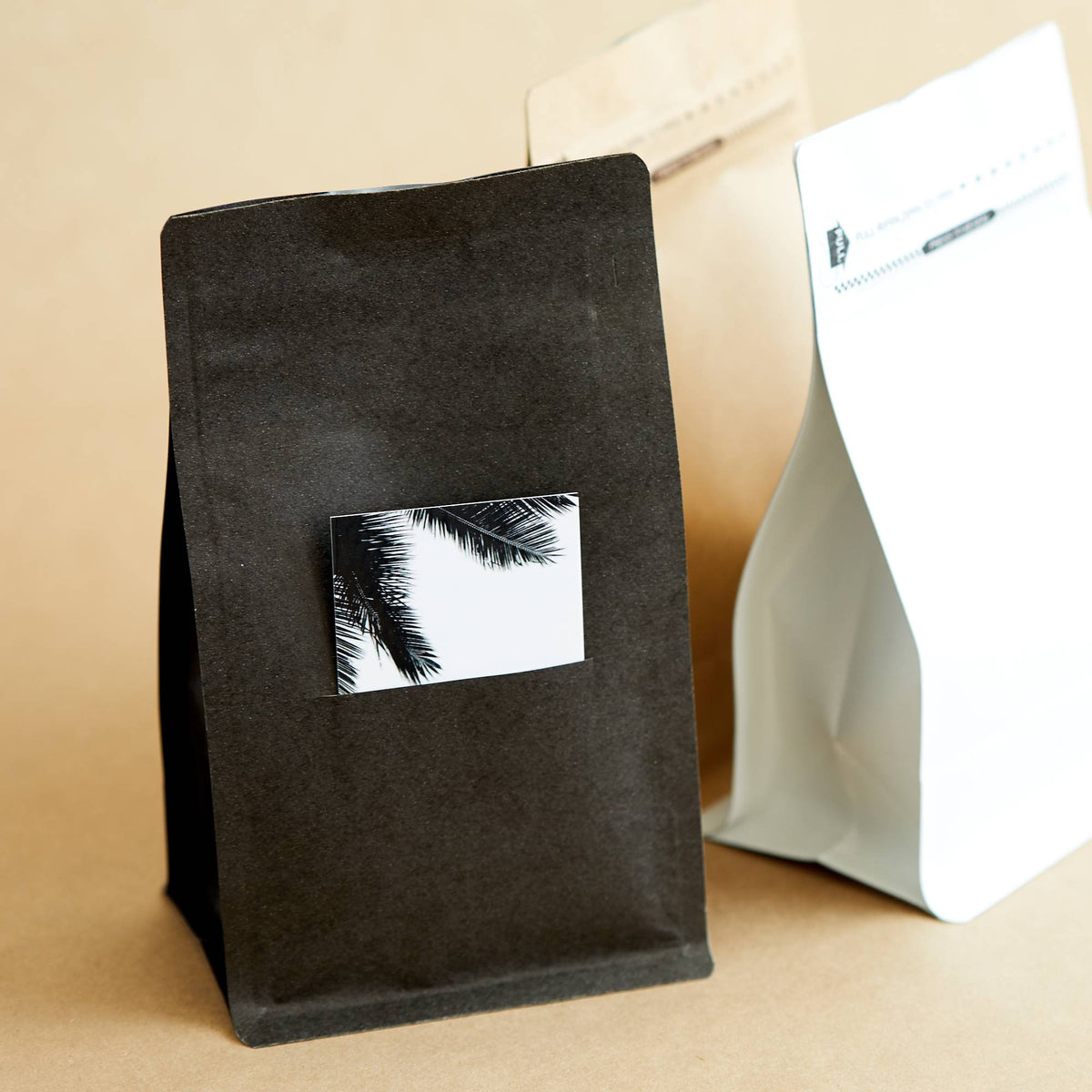 Matte black stand-up pouch with a palm print card, beside kraft and white pouches