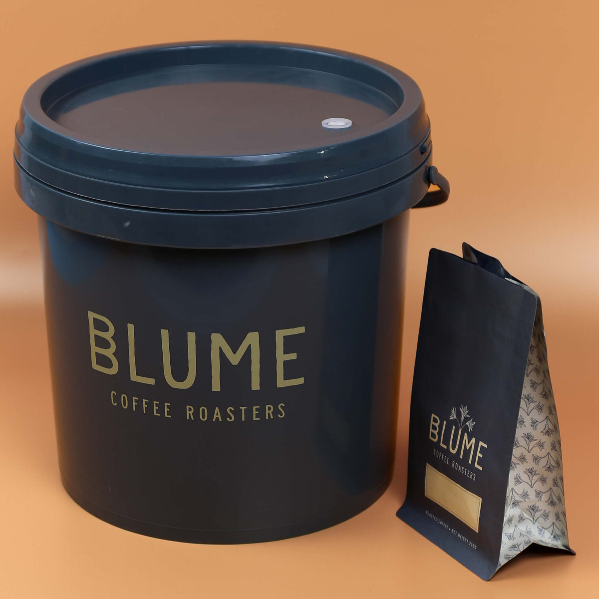 Dark grey printed coffee bucket with lid beside a matching coffee pouch on a tan background