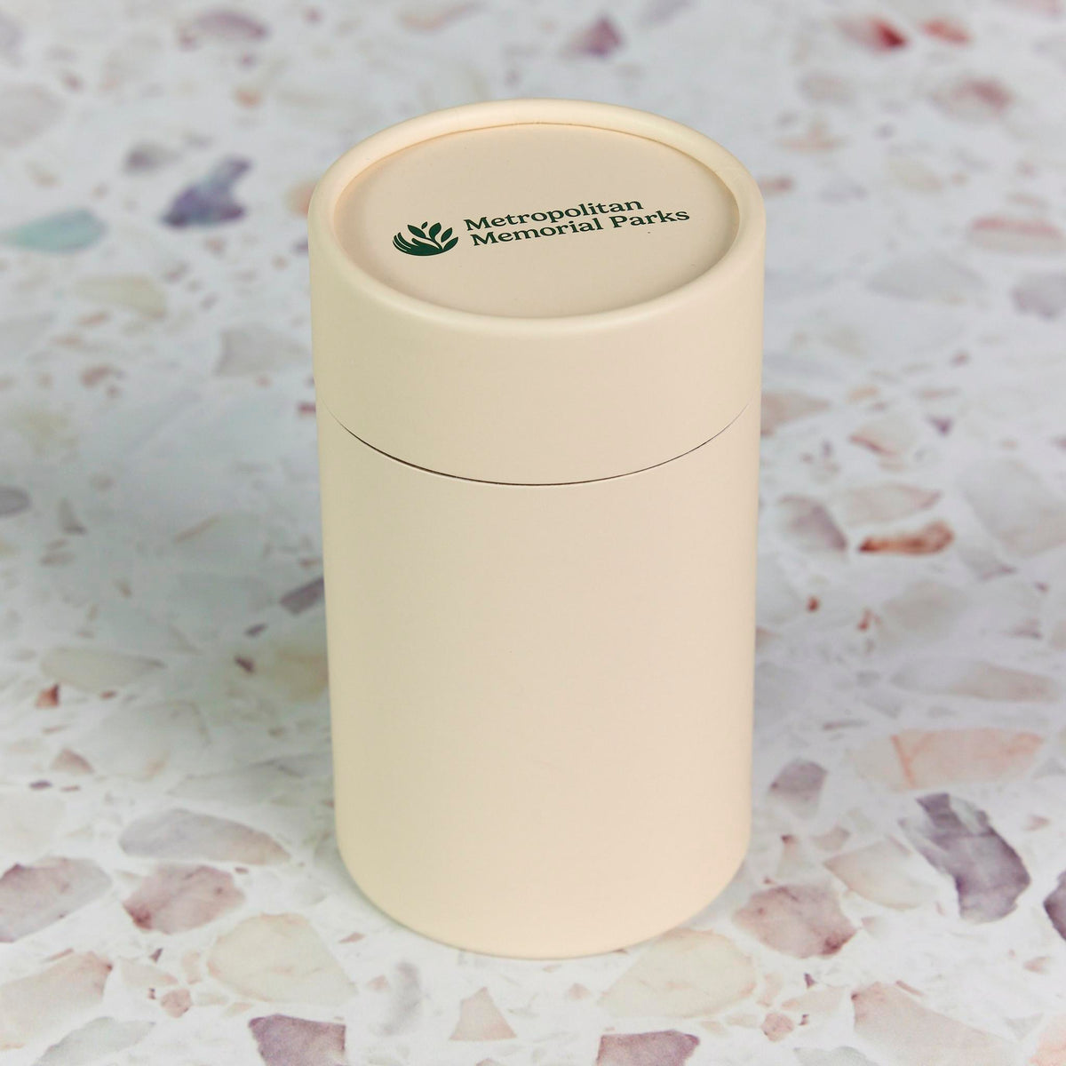 Cream packaging cylinder printed with Metropolitan Memorial Parks on the lid, on a terrazzo surface