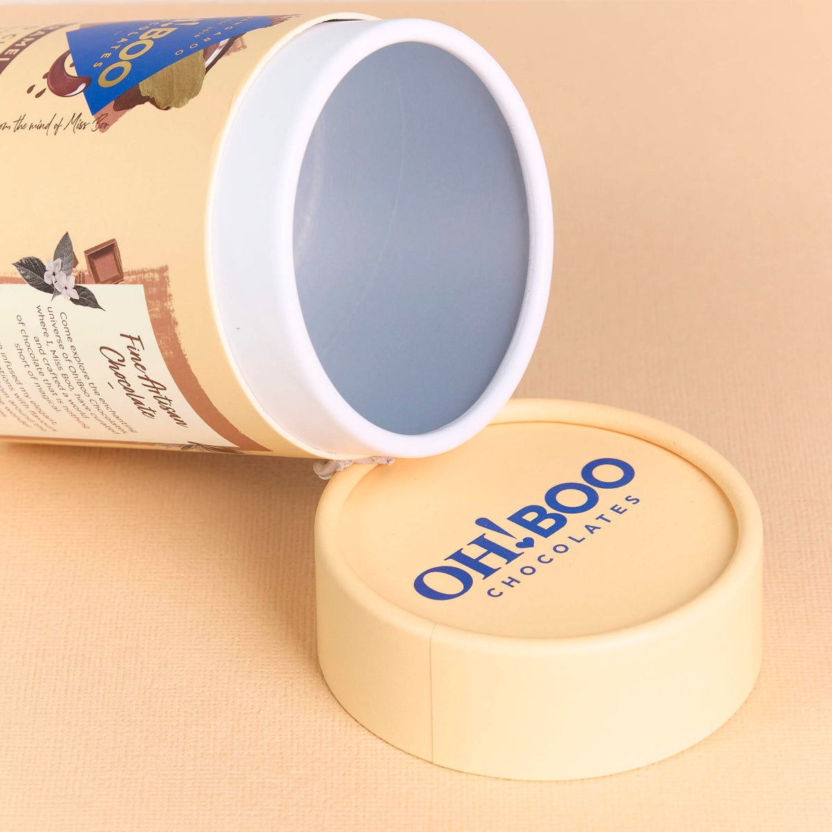 Open custom-printed cream packaging cylinder and lid printed with Oh! Boo Chocolates on a beige background