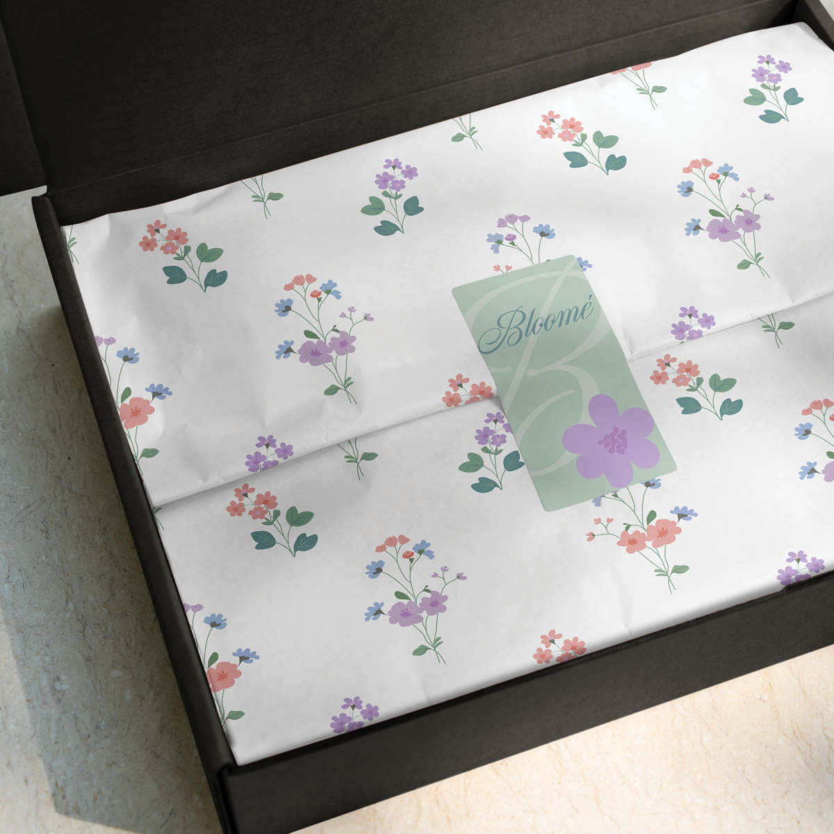 White floral-patterned tissue paper sealed with a green sticker inside an open black box