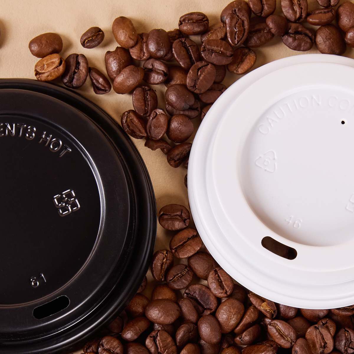 Black and white takeaway coffee cup lids on a bed of roasted coffee beans