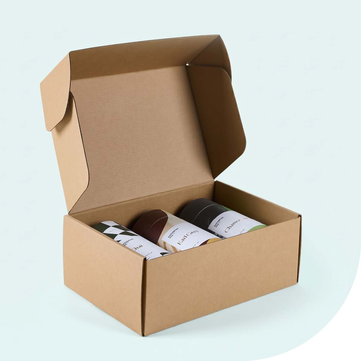 Open plain brown kraft mailer box containing three printed tea cylinders on a pale blue background