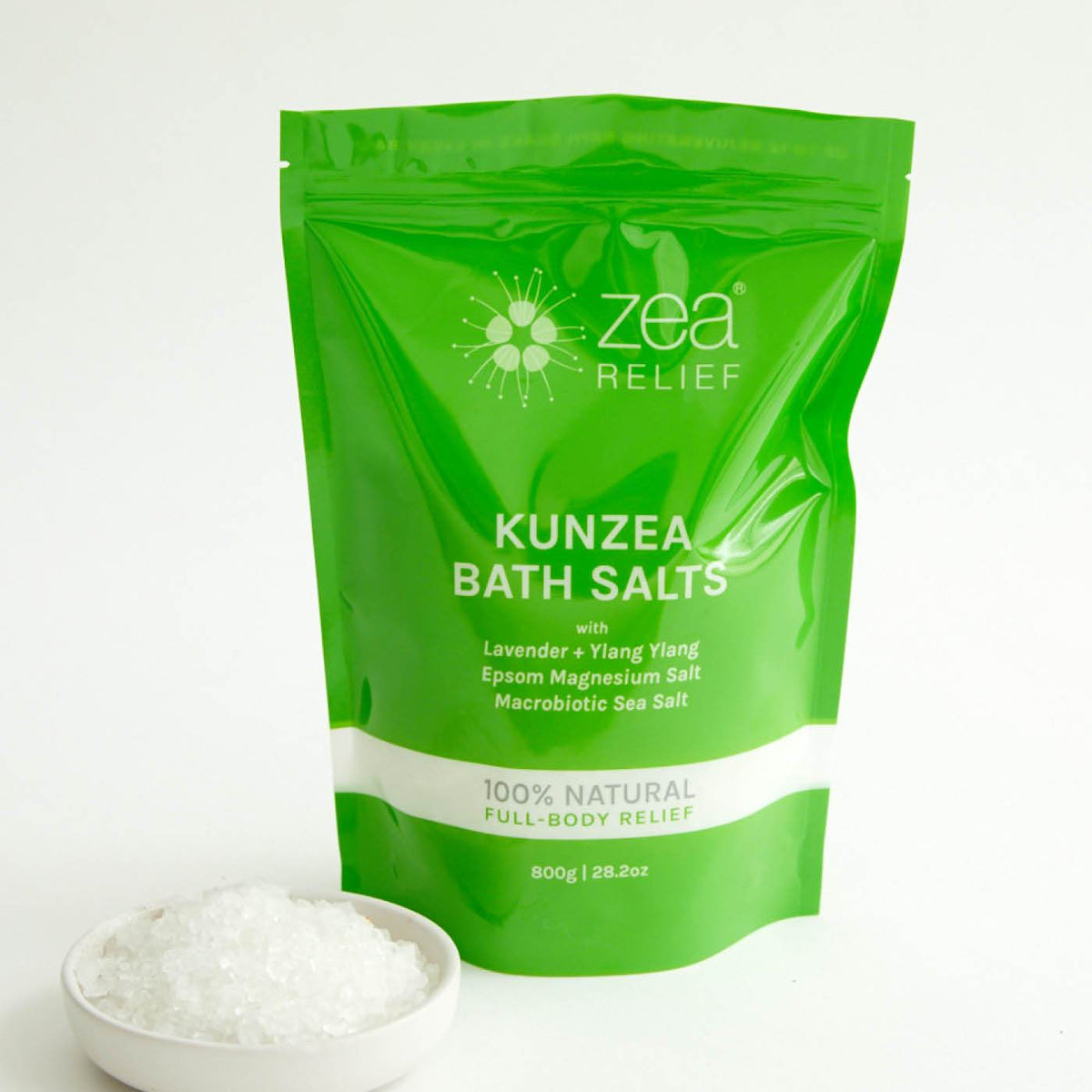 Glossy green printed stand-up pouch beside a small dish of white bath salts on a white surface