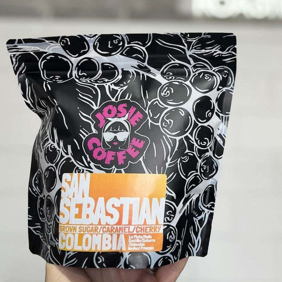 Black stand-up pouch with white coffee cherry illustrations and a colourful product label, held in a hand