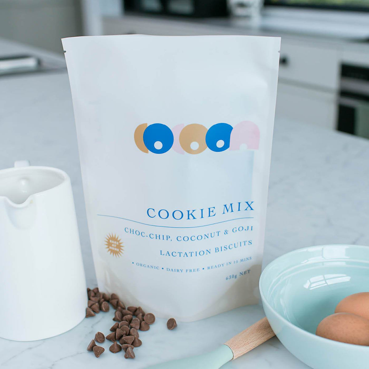 White matte stand-up pouch with printed cookie mix design on a kitchen bench beside baking ingredients