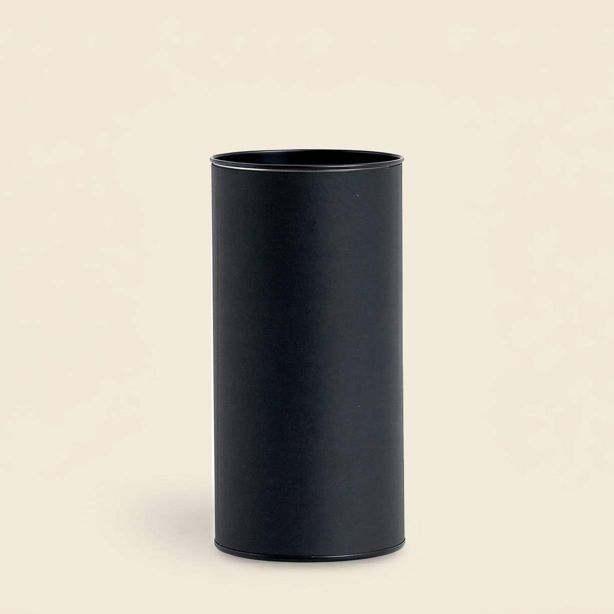 Plain matte black packaging cylinder standing upright against a beige background