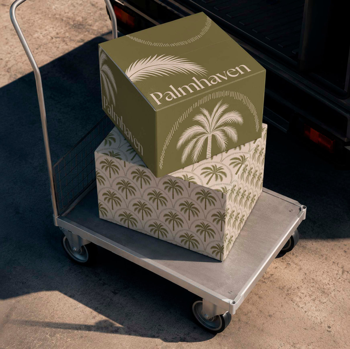 Two shipping cartons with olive green palm tree designs stacked on a flatbed trolley beside an open van