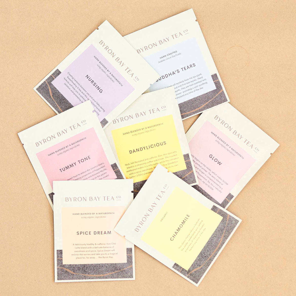 Custom printed white tea sachets with pastel colour accents fanned out across a kraft cardboard background