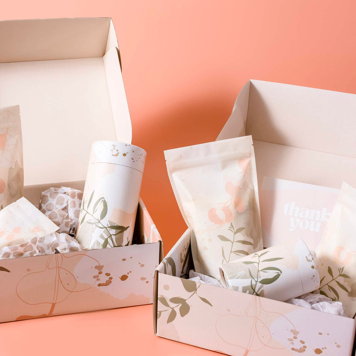 Open mailer boxes containing matching botanical-print stand-up pouches and cylinders on a peach background