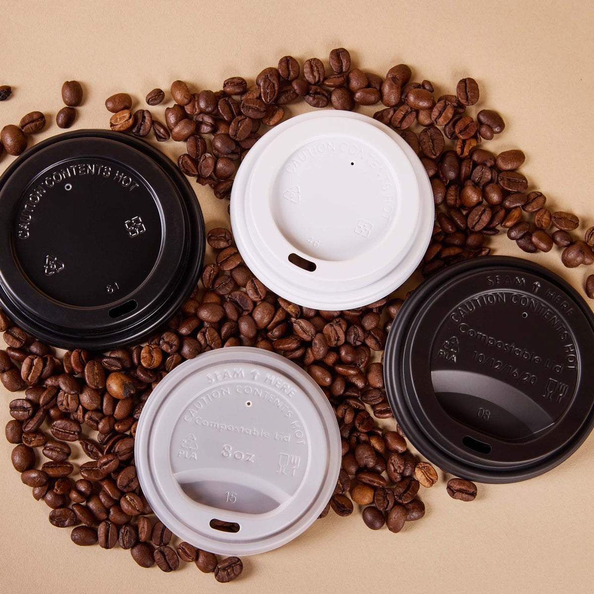 Four black and white takeaway coffee cup lids arranged on a bed of roasted coffee beans on a beige background