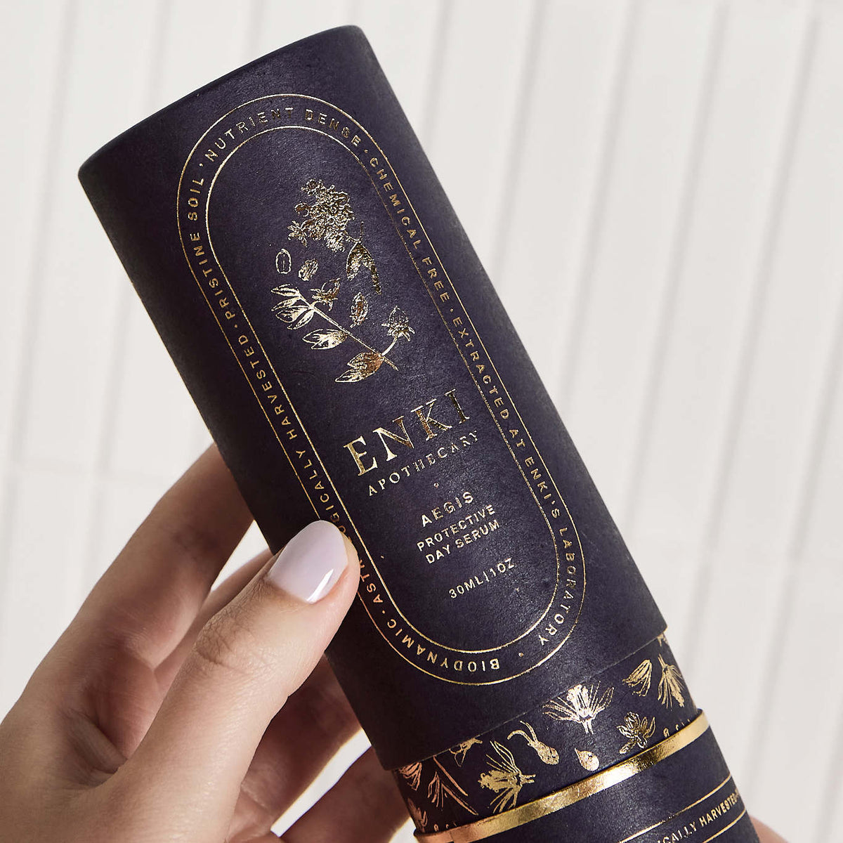 Matte black packaging cylinder with gold foil botanical print and text, held against a white background