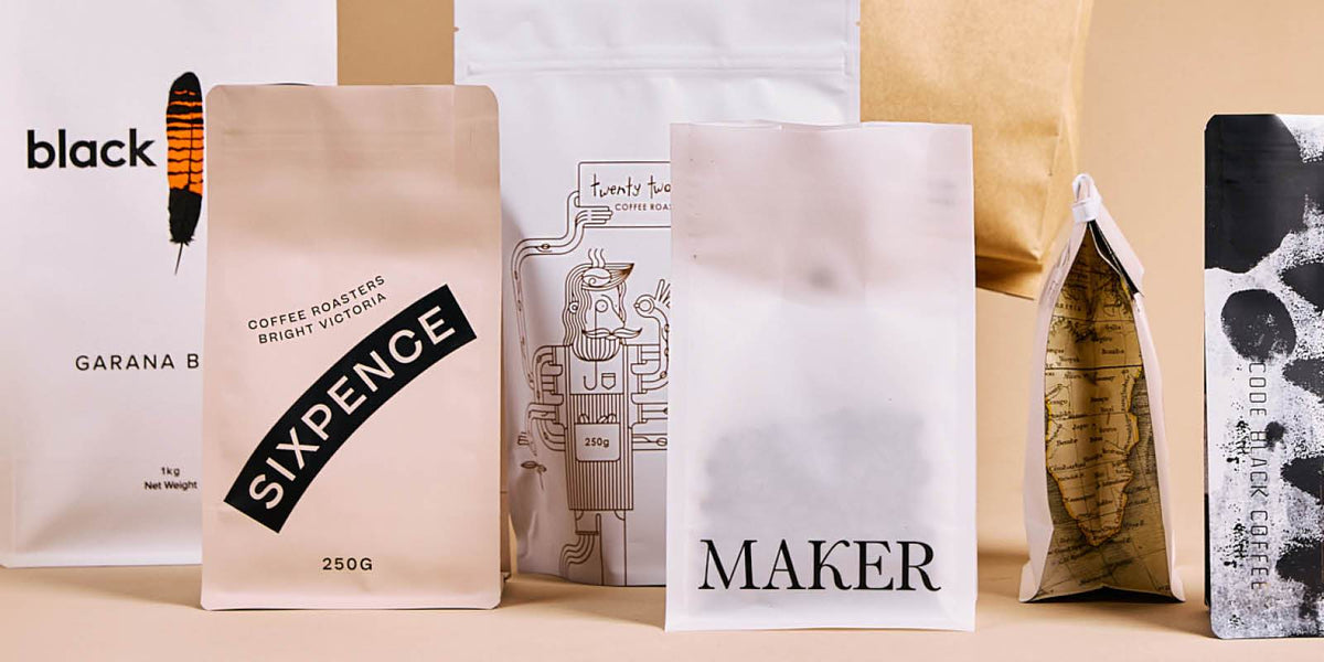 Custom-printed coffee pouches with various graphic designs standing in a row on a neutral background