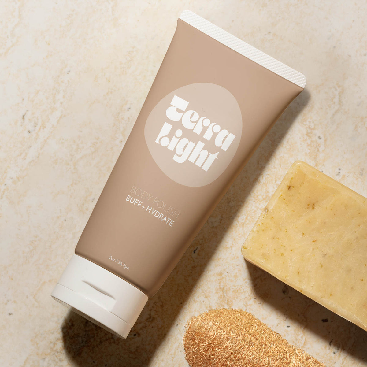 Matte tan cosmetic tube with custom white print and flip cap, set on a beige stone surface with a soap bar