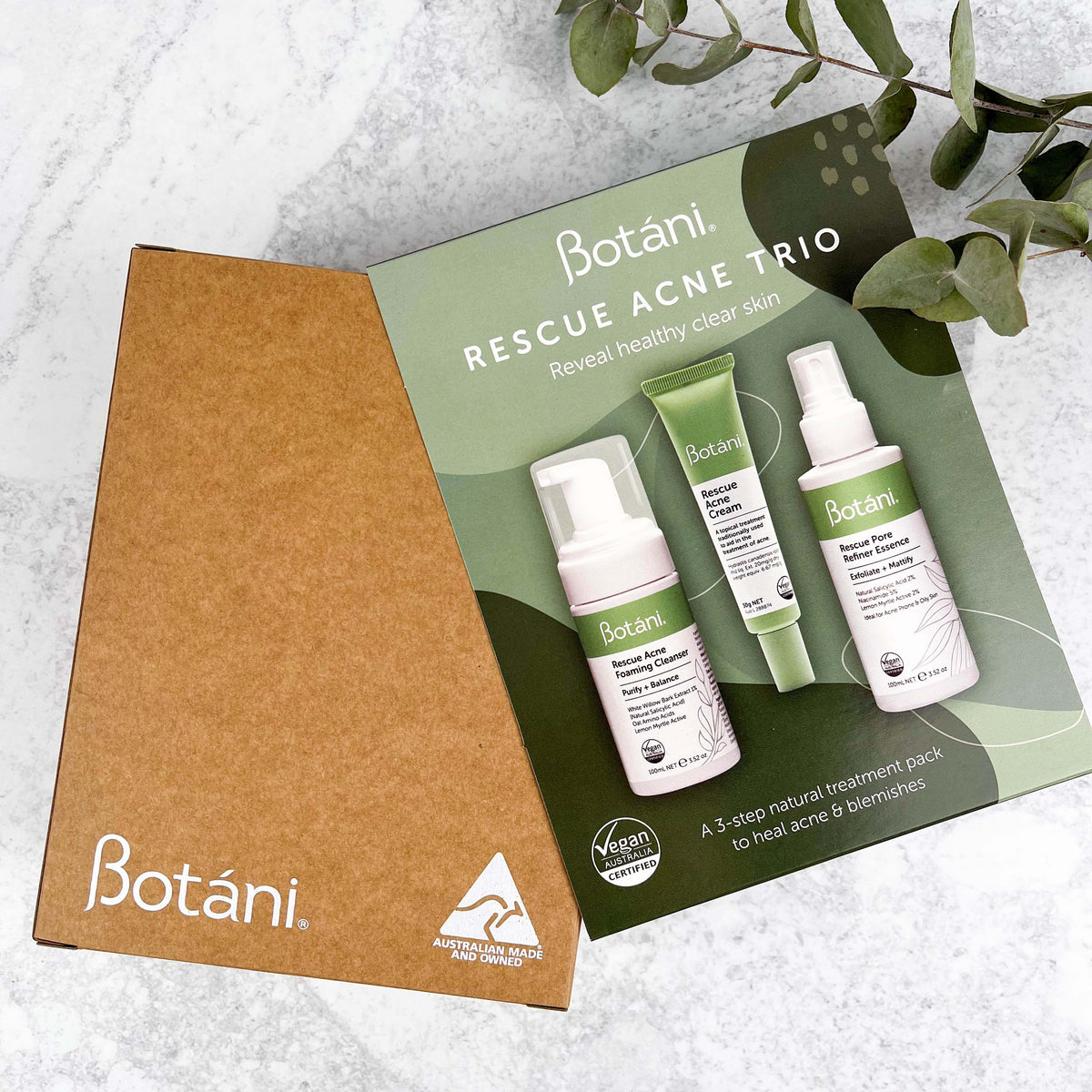 Custom printed kraft mailer box and branded green packaging sleeve on a marble surface with gum leaves