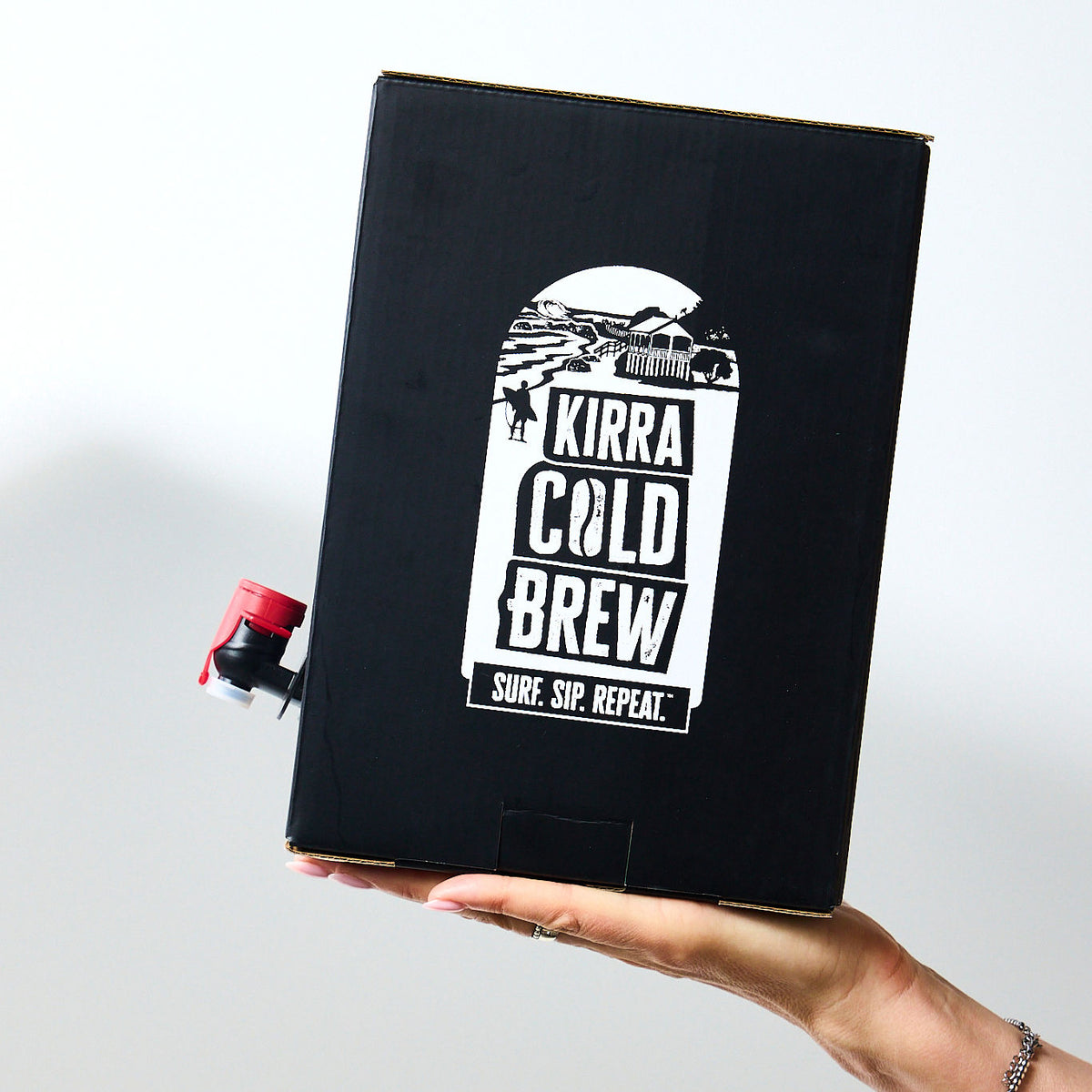 Black printed bag-in-box carton with a red dispensing tap, held in a hand against a white background