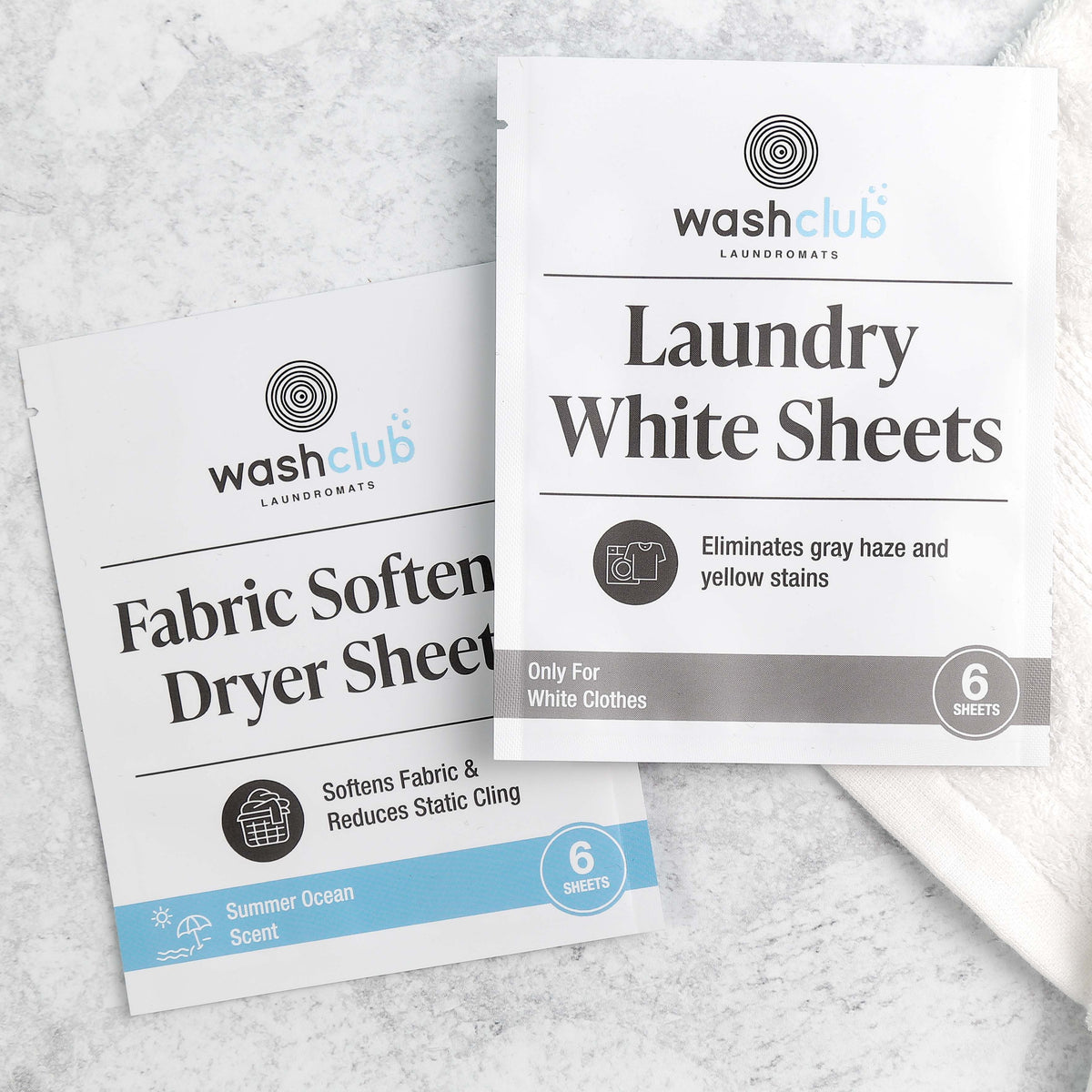 Two custom-printed white sachets for laundry sheets resting on a light marble surface next to a towel