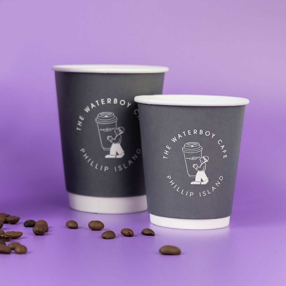 Two grey paper coffee cups with custom white branding on a purple background with scattered coffee beans