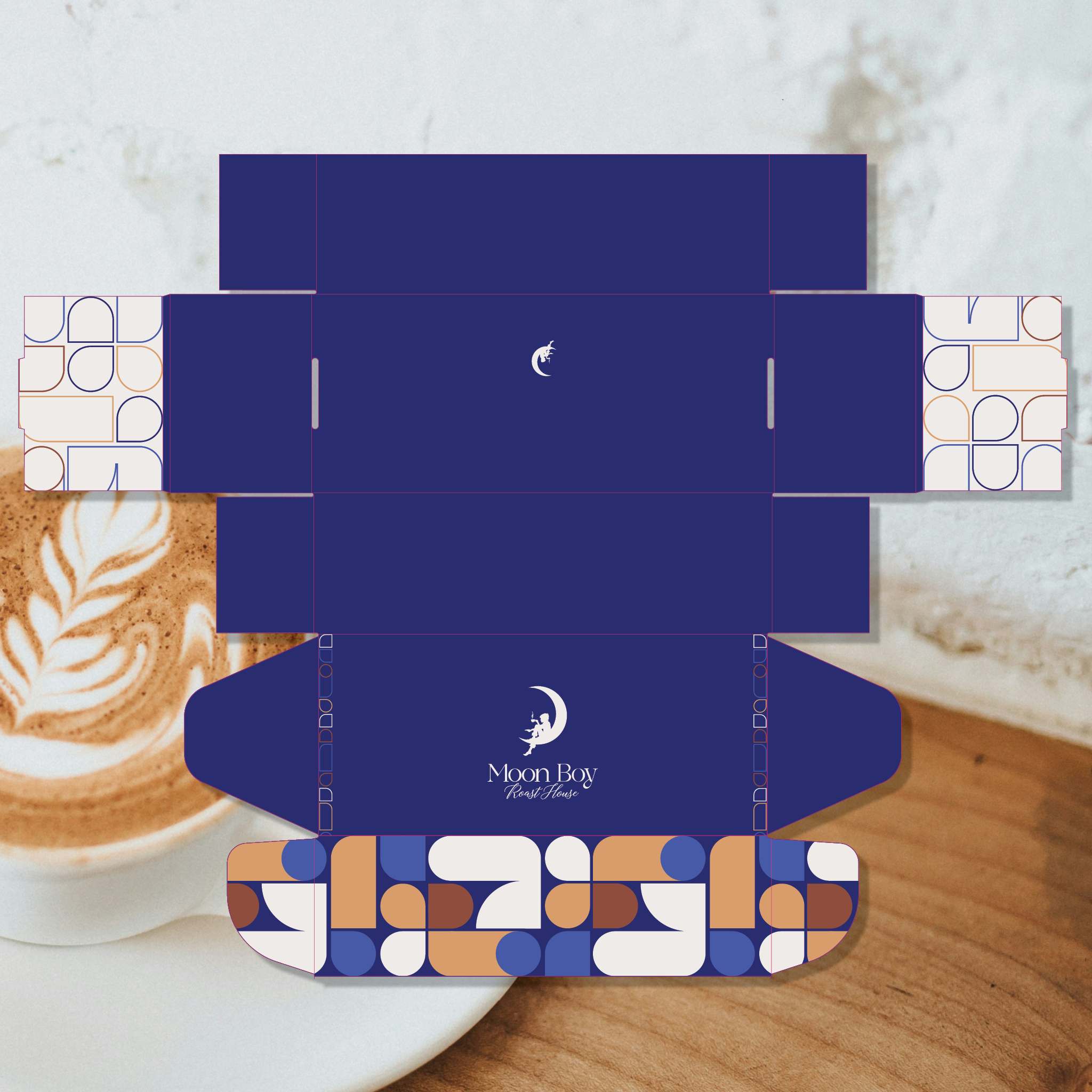 A flat cardboard box template with a deep navy blue center and geometric patterned flaps in blue, beige, brown, and white, displayed over a coffee cup on a wooden surface.