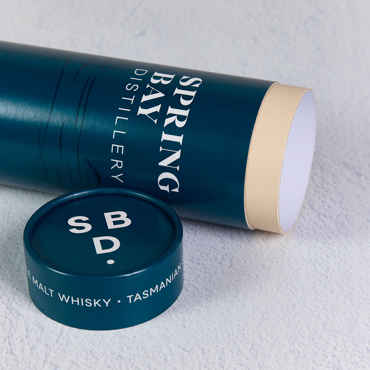 Deep teal custom-printed cardboard cylinder and matching lid with white branding on a light textured surface