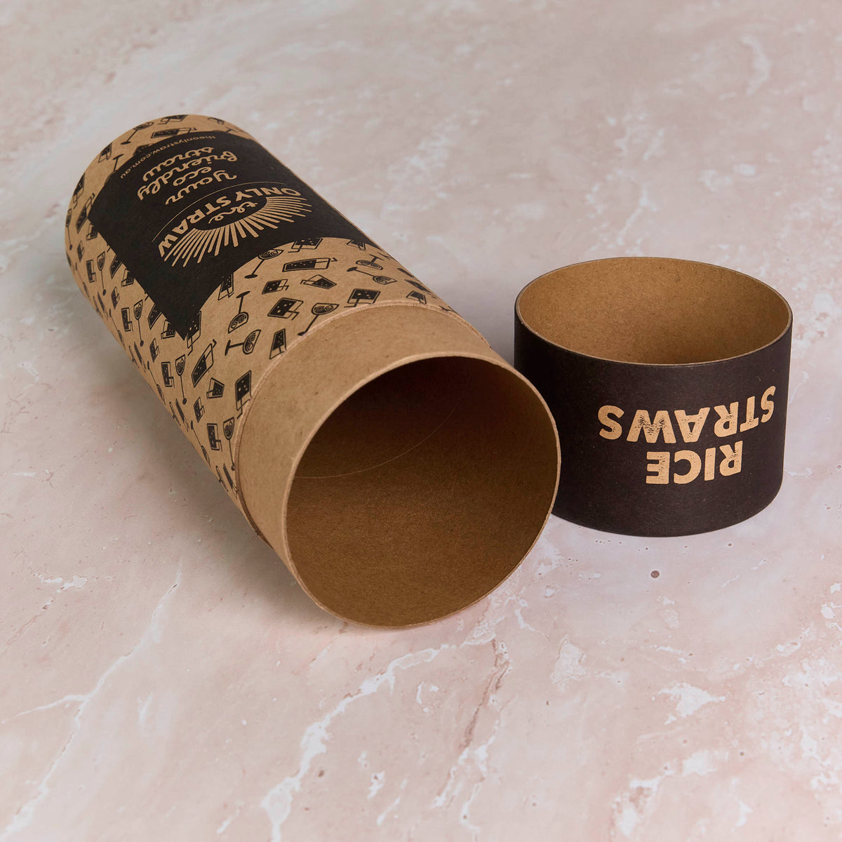 Open kraft cardboard cylinder with custom black print and matching black lid resting on a marble surface