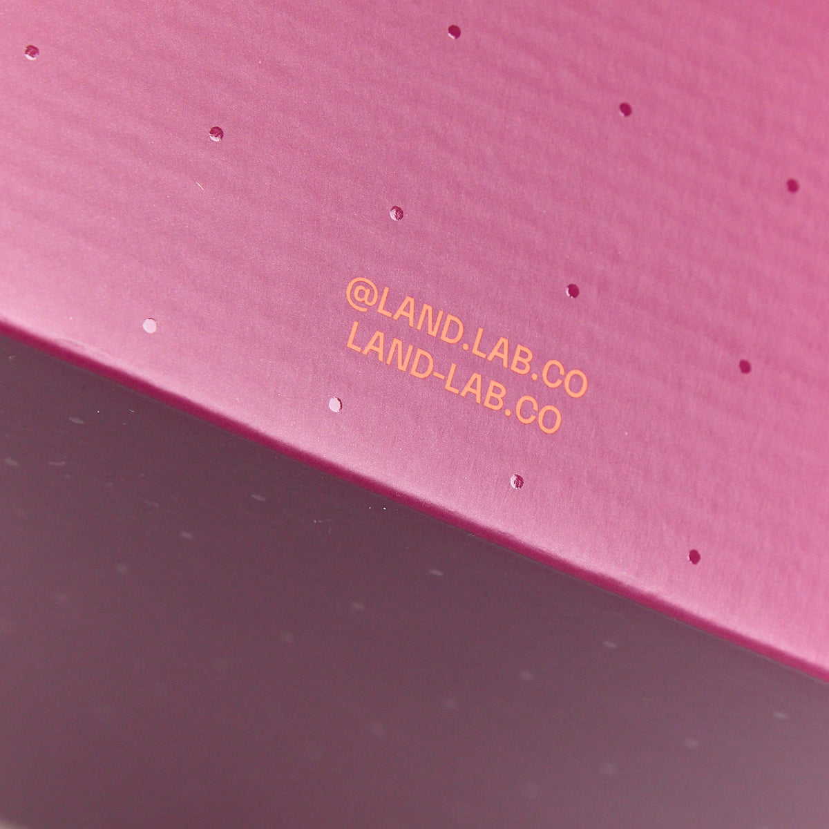 Close-up of a burgundy cardboard box featuring a subtle dot pattern and orange printed text