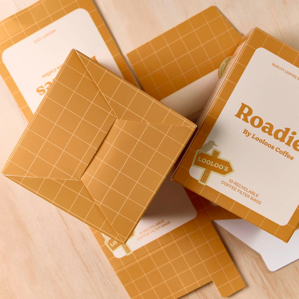 Custom-printed ochre and white cartons with a grid design, showing the interlocking base on a light timber surface