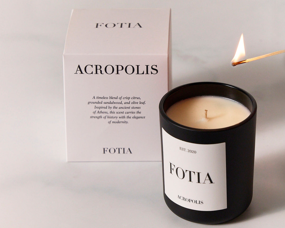 Printed white candle box beside a matte black candle jar with a white label and a lit match