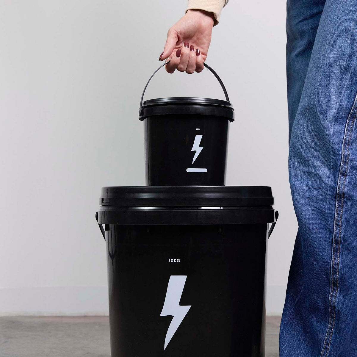 A small black plastic pail held above a larger matching pail, both printed with a white lightning bolt
