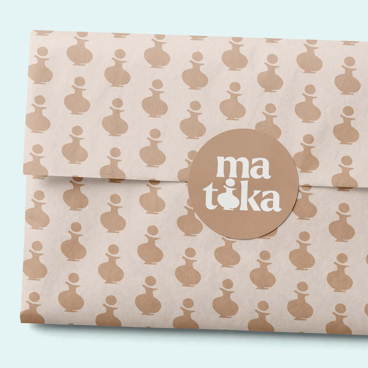 Folded beige tissue paper with a brown bottle pattern, sealed with a round sticker on a light blue background