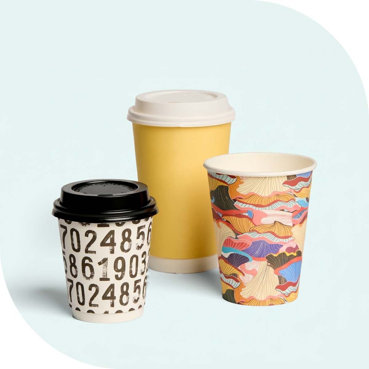 Three takeaway coffee cups: a plain yellow cup, one with printed black numbers, and one with colourful artwork