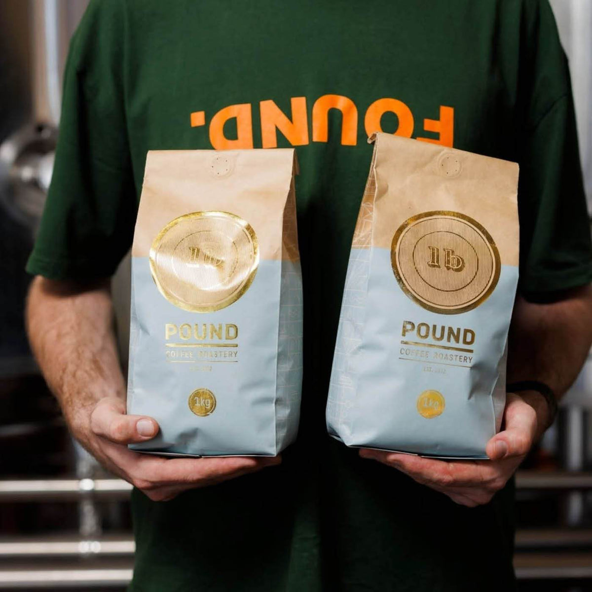 Person holding two kraft paper and light blue coffee bags printed with metallic gold foil logos