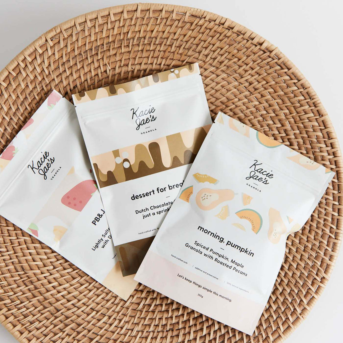 Three custom-printed matte white stand-up pouches with colourful illustrations resting in a woven wicker tray