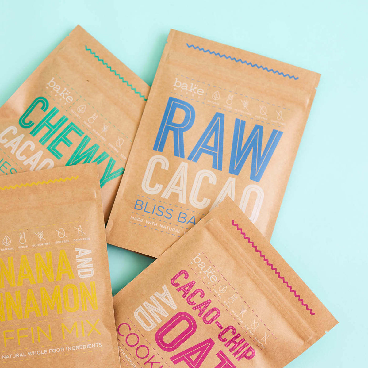 Four brown stand-up pouches printed with colourful text, arranged on a light blue background
