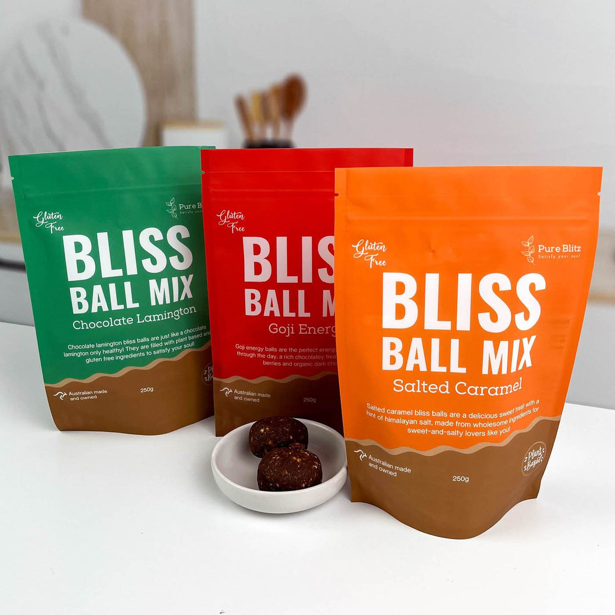 Three custom-printed matte stand-up pouches in green, red and orange beside a small dish of bliss balls on a benchtop