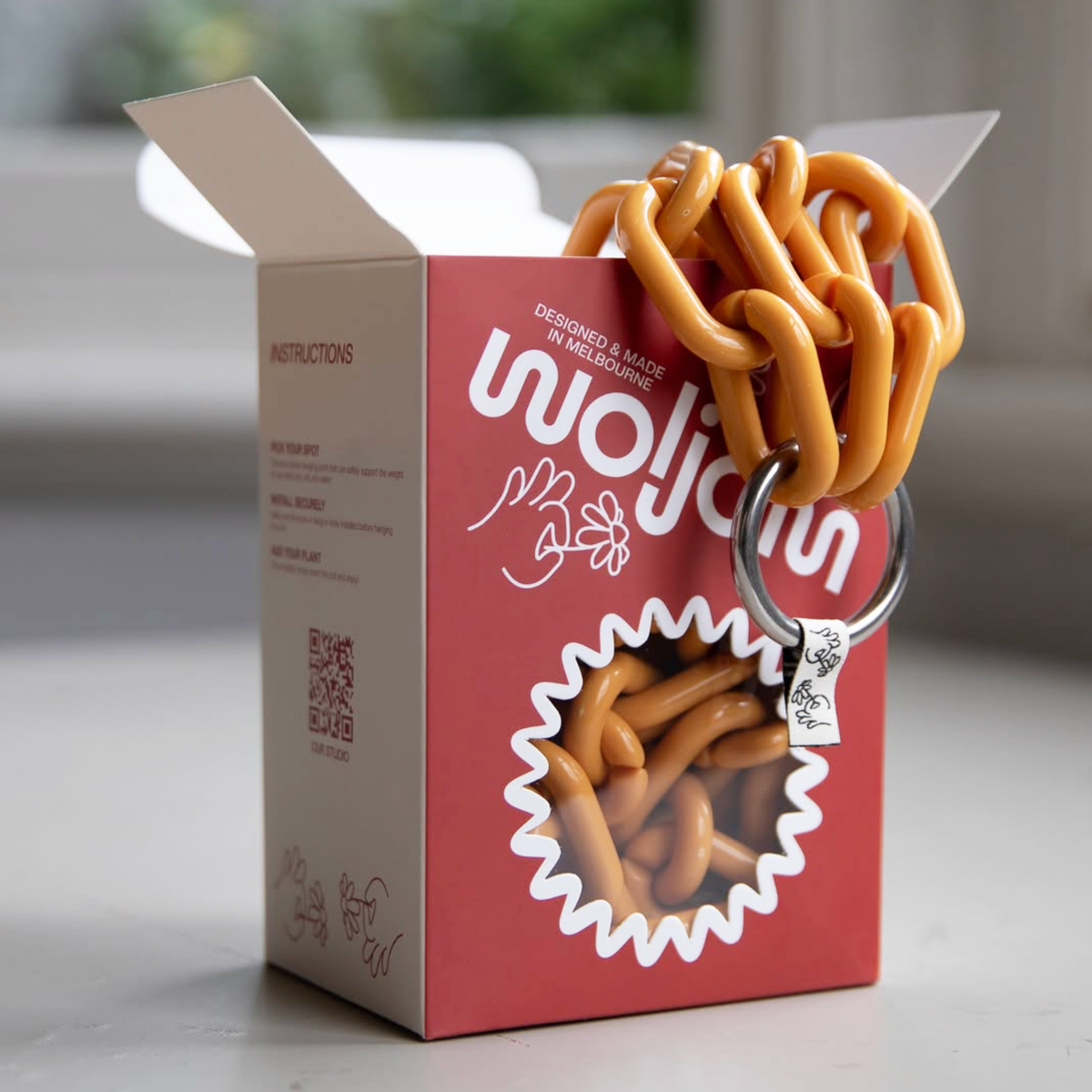Rust-red and white printed carton with a die-cut star window, holding a mustard-yellow plastic chain