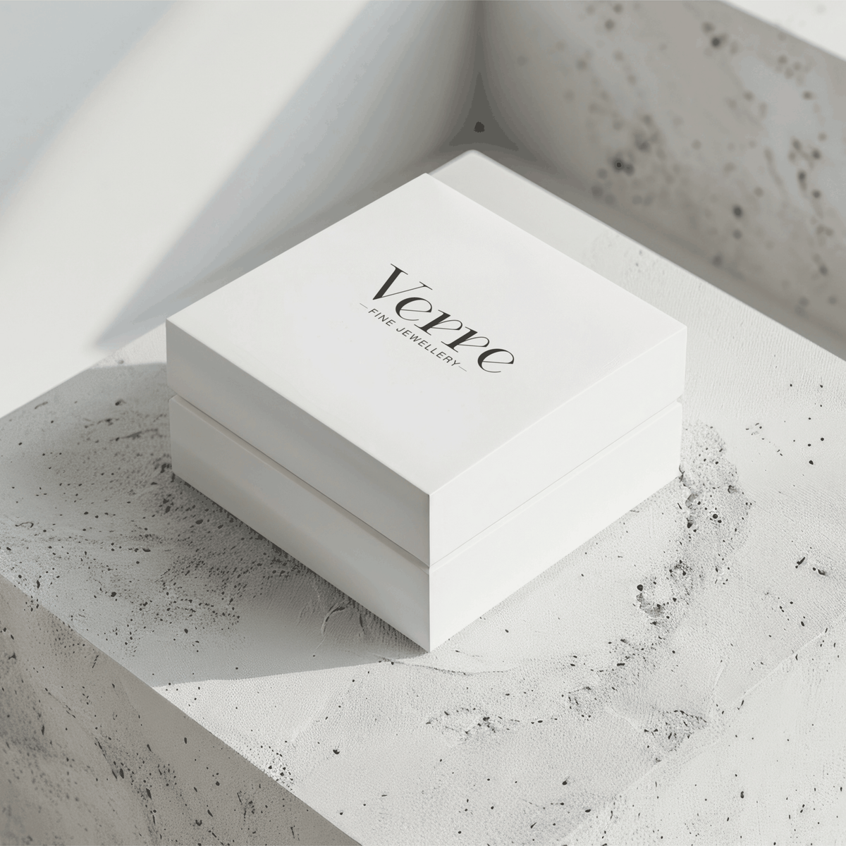 White square jewellery box printed with black Verre branding, resting on a textured concrete plinth